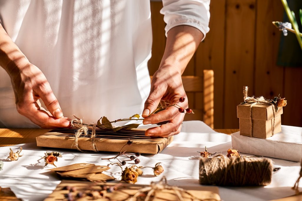 Woman decorating wrapped gifts with recycled paper with dried flowers. Natural aesthetic.