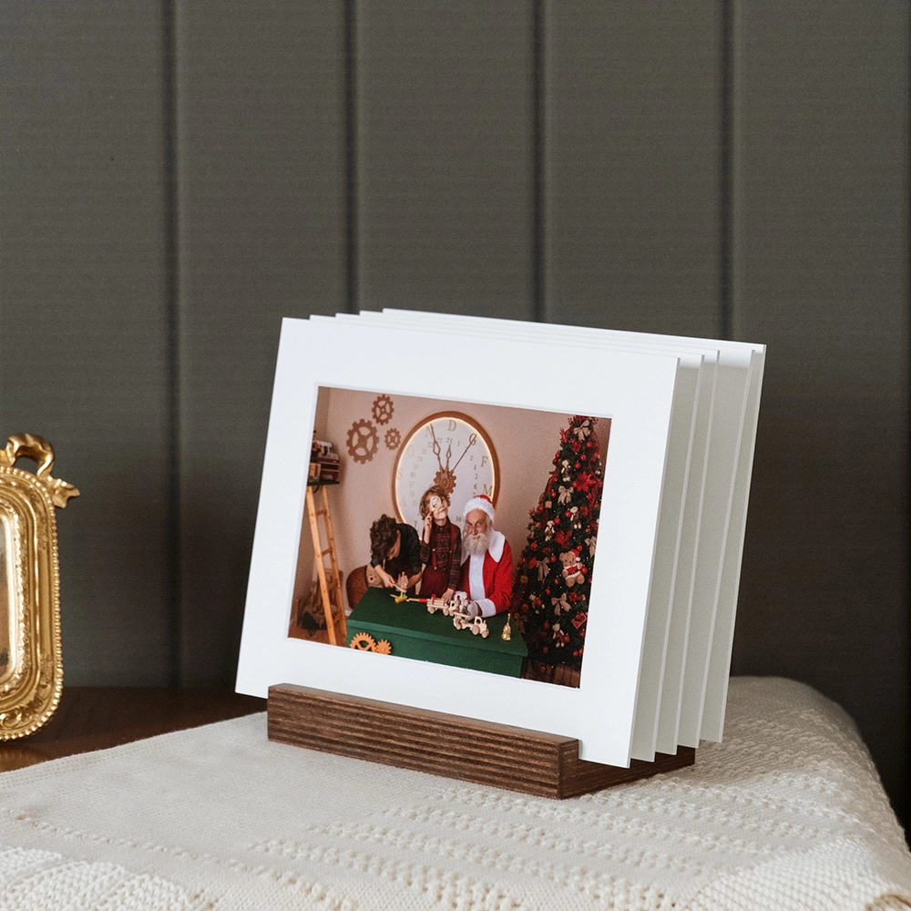 Soporte de madera multifotos con passepartout blanco. Exhibe 5 fotos favoritas en papel lustre. Base de madera nogal con 5 ranuras, formato 20x15 cm. Presentación moderna y elegante para recuerdos navideños y familiares.