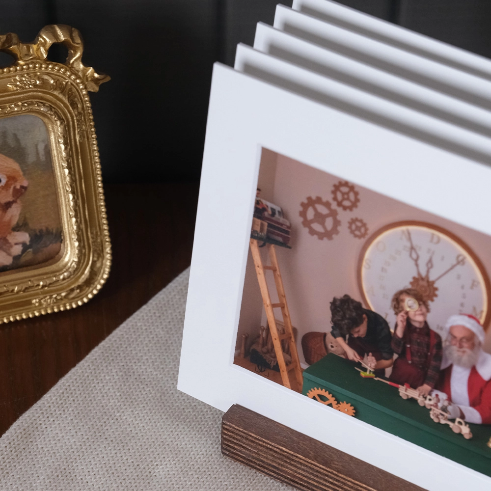 Soporte de madera multifotos con passepartout blanco. Exhibe 5 fotos favoritas en papel lustre. Base de madera nogal con 5 ranuras, formato 20x15 cm. Presentación moderna y elegante para recuerdos navideños y familiares.