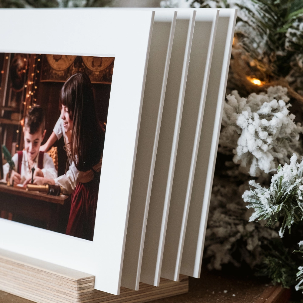 Soporte de madera multifotos con passepartout blanco. Exhibe 5 fotos favoritas en papel lustre. Base de madera nogal con 5 ranuras, formato 20x15 cm. Presentación moderna y elegante para recuerdos navideños y familiares.