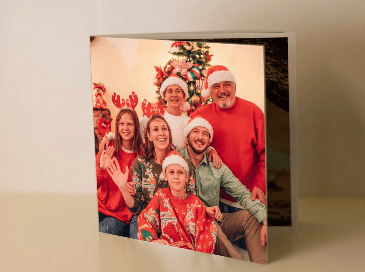 Minibook personalizado para Navidad abierto sobre una mesa navideña, mostrando en su interior fotografías familiares impresas con colores vivos y acabado profesional, junto a decoración navideña como luces cálidas, ramas de pino y lazos rojos, destacando su formato compacto y elegante presentación como detalle regalo.