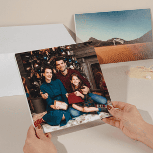 Minibook personalizado para Navidad abierto sobre una mesa navideña, mostrando en su interior fotografías familiares impresas con colores vivos y acabado profesional, junto a decoración navideña como luces cálidas, ramas de pino y lazos rojos, destacando su formato compacto y elegante presentación como detalle regalo.